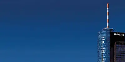 Blauer Himmel ist im Großteil des Bildes zu sehen. auf der rechten Seite ist die Spitze eines verglasten und runden Hochhauses zu sehen. Auf dem Dach ist ein weiß-rot-gestreifter Mast zu sehen. Bild zur Verfügung gestellt von der Landesbank Hessen-Thüringen, Frankfurt